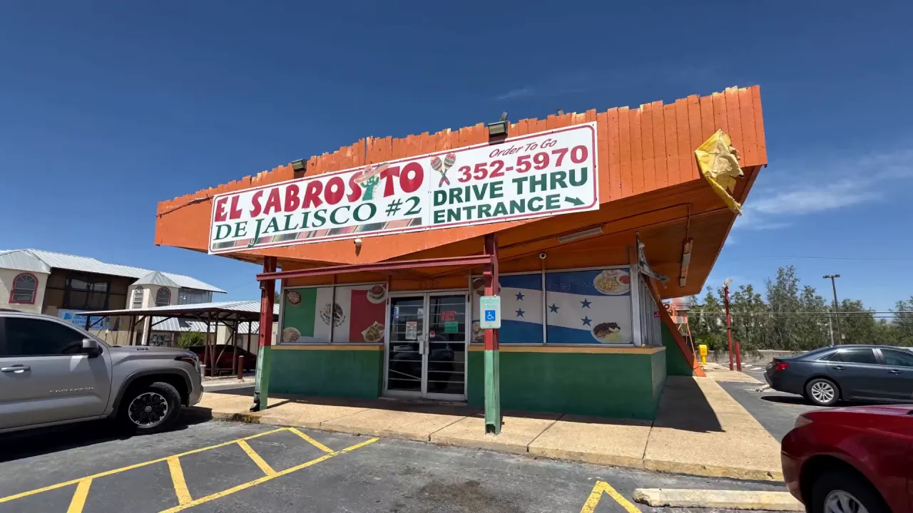 The storefront of El Sabrosito de Jalisco #2, with the Mexican flag mural left of the door and the Honduran flag mural right of it.