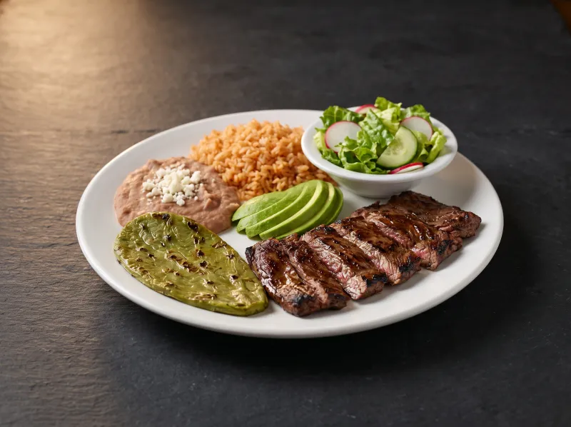 A carne asada plate with rice, refried beans, nopalitos and avocado.